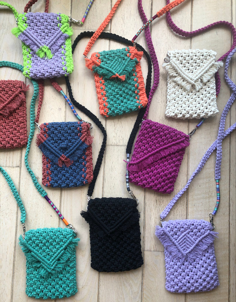 Nine colorful crocheted crossbody bags with fringe details. The bags are made of cotton cord and have a variety of colors, including purple, green, white, red, blue, pink, black, and light purple.